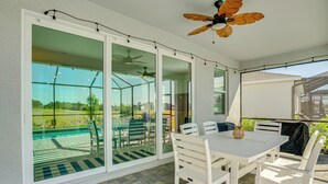 A covered patio with a table and chairs, a ceiling fan, and a view of a swimming pool and greenery. - Golfers Dream Ibis Landing Golf (Lehigh Acres)