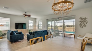 A spacious living room with a large dining table, blue sofas, and a chandelier. - Golfers Dream Ibis Landing Golf (Lehigh Acres)