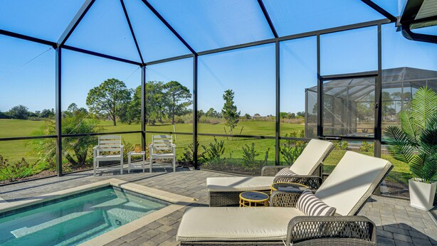 A covered outdoor area with a pool, lounge chairs, and a view of the surrounding landscape. - Golfers Dream Ibis Landing Golf (Lehigh Acres)