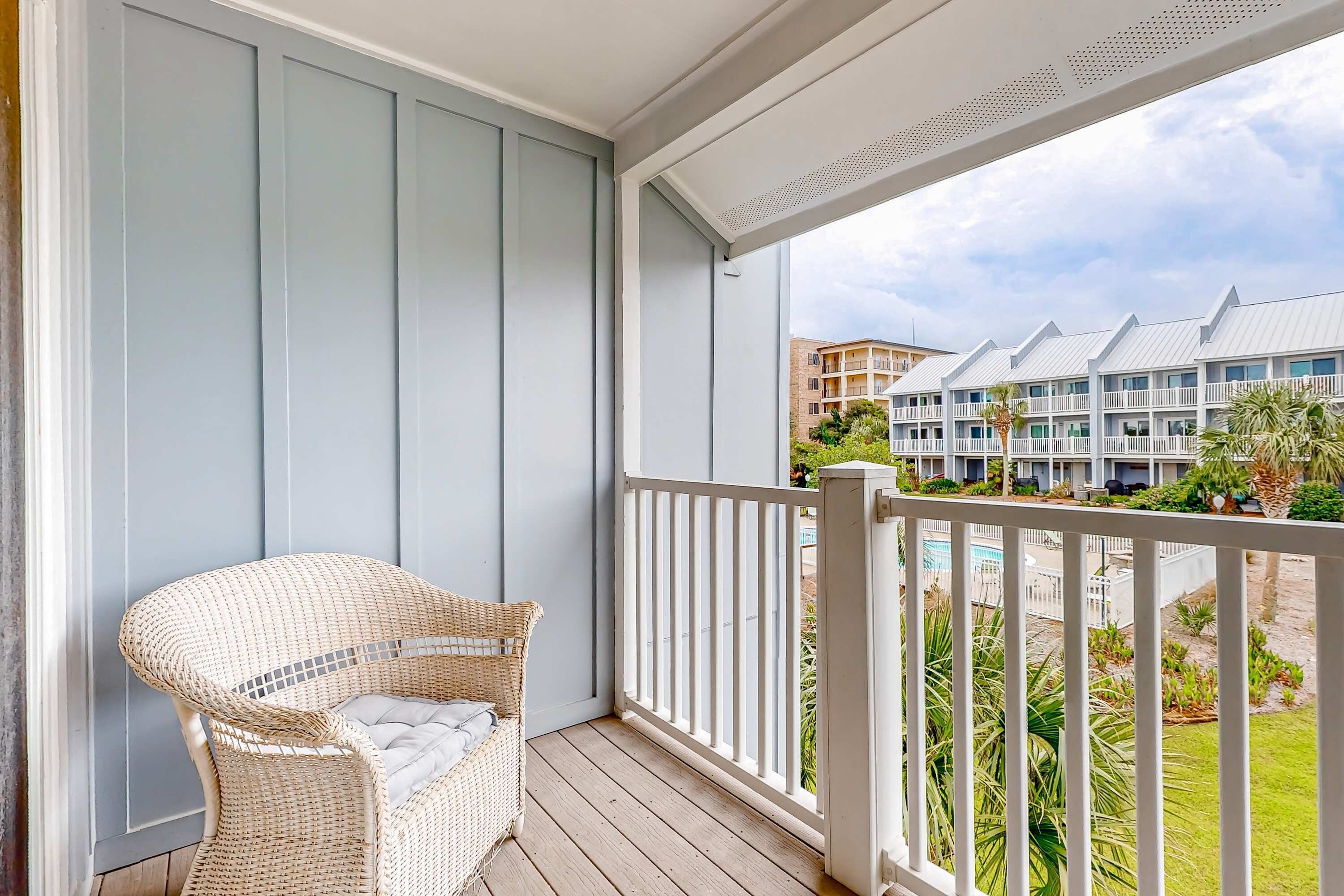 A balcony with a wicker chair, a white railing, and a view of a hotel building with multiple balconies.