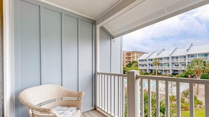 Ein Balkon mit Korbstuhl, weißer Brüstung und Blick auf ein Hotelgebäude mit mehreren Balkonen.