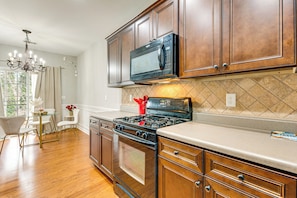 A modern kitchen with wooden cabinets, a stainless steel microwave, a gas stove, and a dining area with a glass table and chairs. - Community Pool! East ATL Base Near Mercedes-benz (Atlanta)