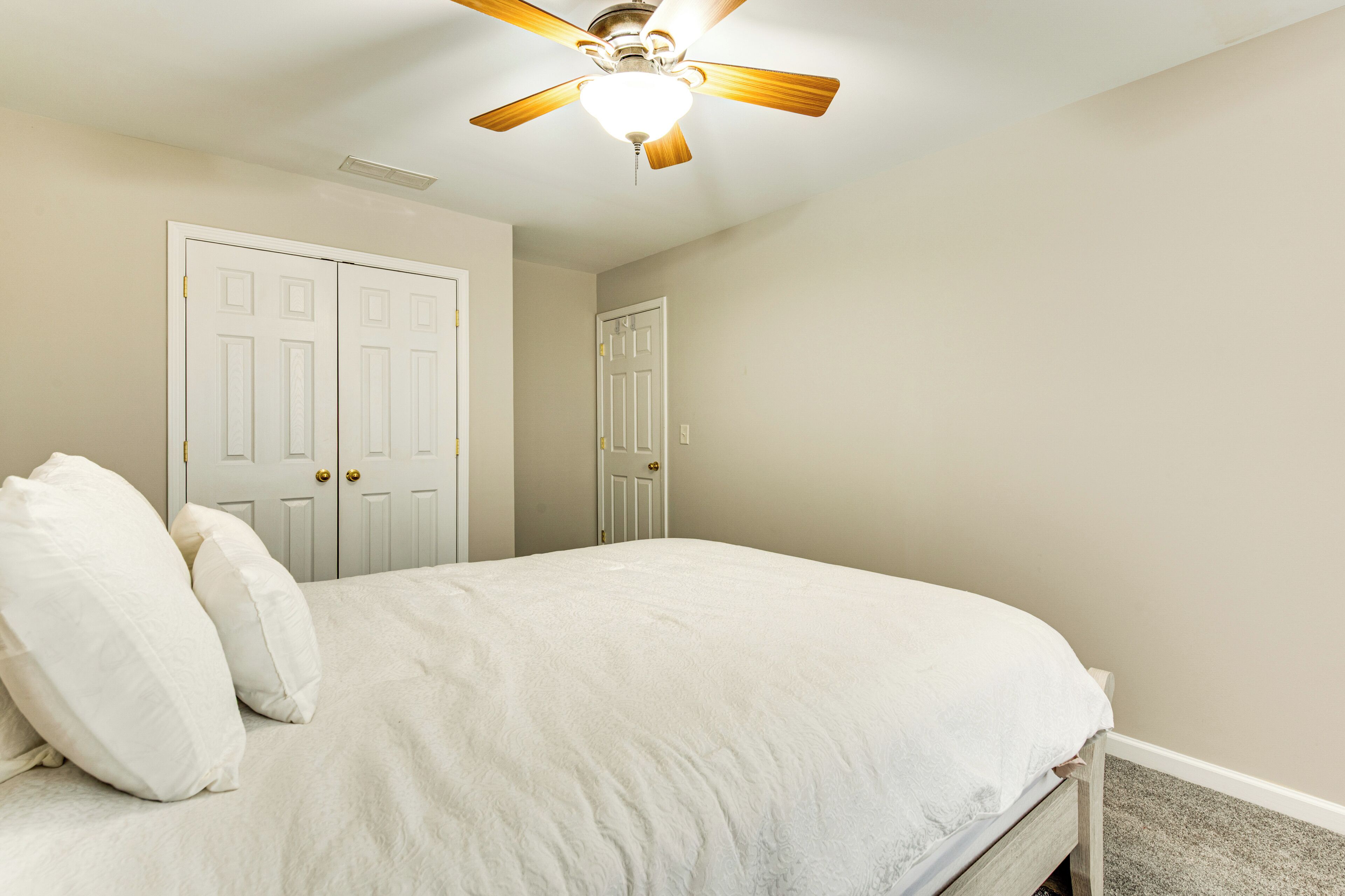 Une chambre à coucher avec un lit, deux portes blanches et un ventilateur de plafond.