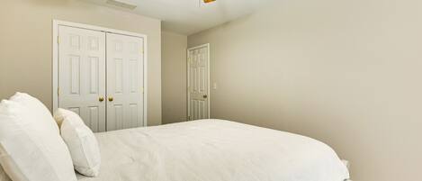 A bedroom with a bed, two white doors, and a ceiling fan.