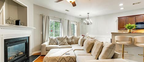 A modern living room with a fireplace, a sectional sofa, a ceiling fan, and a kitchen area with bar stools.