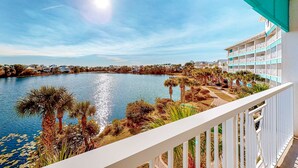 Une vue depuis un balcon donnant sur un lac, avec des palmiers et un immeuble doté de nombreux balcons.