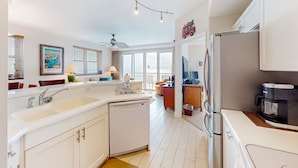 Una cocina moderna con armarios blancos, lavavajillas, refrigerador y cafetera.