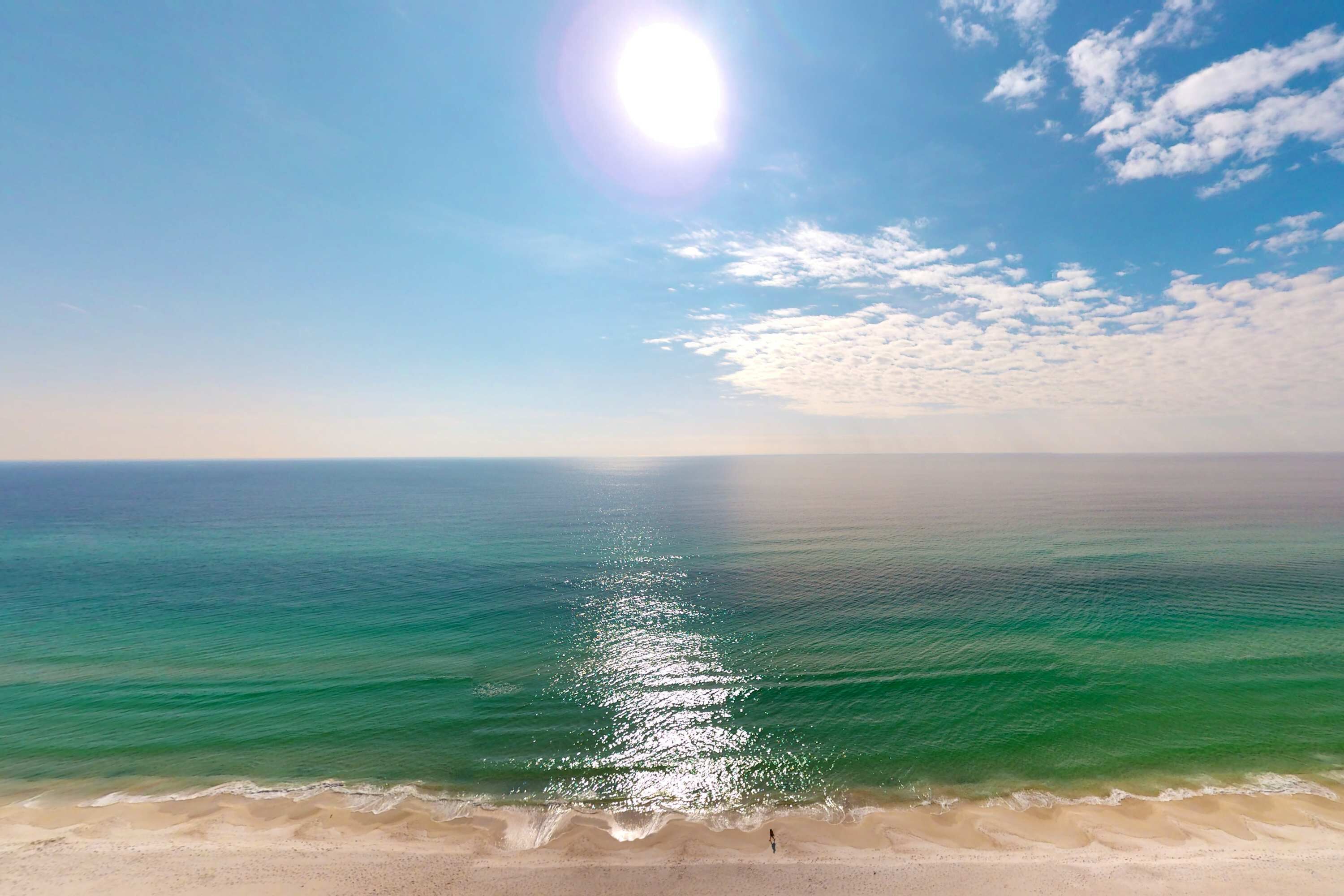 Ein Strand mit klarem türkisblauem Wasser, das die Sonne reflektiert, einem sandigen Ufer und blauem Himmel.