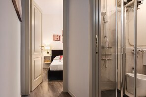 Una camera d'albergo con un letto, un comodino, una lampada e un angolo doccia con porta in vetro.