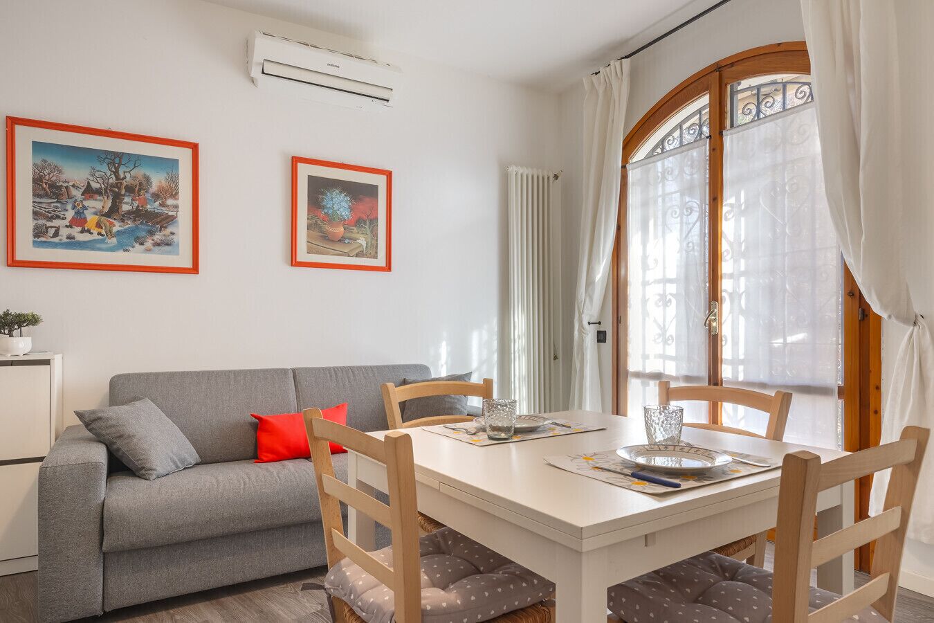Una sala de estar acogedora con un sofá gris, un cojín rojo y dos cuadros enmarcados en la pared.