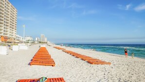 Een strand met rijen houten ligbedden, een heldere lucht en een gebouw op de achtergrond.