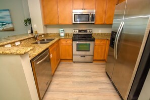 A modern kitchen with granite countertops, stainless steel appliances, wooden cabinets, and a dishwasher. - Beautiful west-facing home in Gulf-front building with pool & hot tub (Panama City Beach)