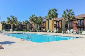 A swimming pool with lounge chairs and palm trees, surrounded by multi-story buildings with balconies. - Beachy townhome w/ shared pool, tennis, & shuffleboard (Panama City Beach)