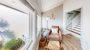 Ein Zimmer mit großem Fenster, einem Sessel, einem kleinen Tisch, einer Lampe und einer Treppe.