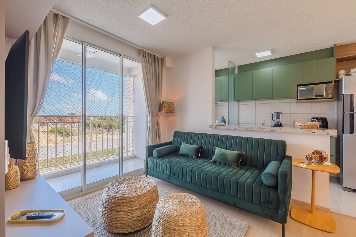 A modern living room with a green sofa, a flat-screen TV, and a balcony with a view.
