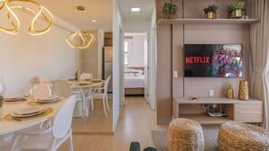 A modern hotel room with a dining area, a TV displaying the Netflix logo, and a bed in the background. - Mirante #406 - Two Bedroom Apartment by Carpediem (Fortaleza)