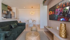 A modern living room with a green sofa, a dining table with chairs, a TV mounted on the wall, and a kitchen area with a microwave and refrigerator. - Mirante #406 - Two Bedroom Apartment by Carpediem (Fortaleza)