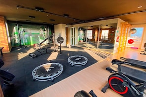 Ein Fitnessstudio mit Trainingsgeräten, darunter Laufbänder und ein Ergometer, sowie einer Spiegelwand.