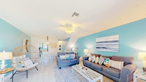 A modern living room with a blue accent wall, a ceiling fan, and a large window. - Relaxing townhome with pool, tennis court, beach access, balcony, patio, & TV (Panama City Beach)