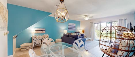 Una sala de estar moderna con una mesa de comedor de vidrio, sillas blancas, un sofá azul y una lámpara esférica colgante.