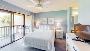 A bedroom with a bed, a TV, a ceiling fan, a balcony, and a nightstand with a lamp. - Relaxing townhome with pool, tennis court, beach access, balcony, patio, & TV (Panama City Beach)