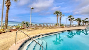 A poolside area with lounge chairs, palm trees, and a view of the ocean. - Gulf-front condo with beautiful sunset views, pool, tiki bar, fitness room & W&D (Panama City Beach)