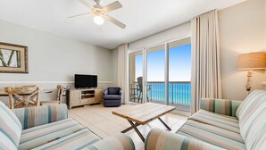 A living room with striped sofas, a wooden coffee table, a television, and a ceiling fan. - Gulf-front condo with beautiful sunset views, pool, tiki bar, fitness room & W&D (Panama City Beach)