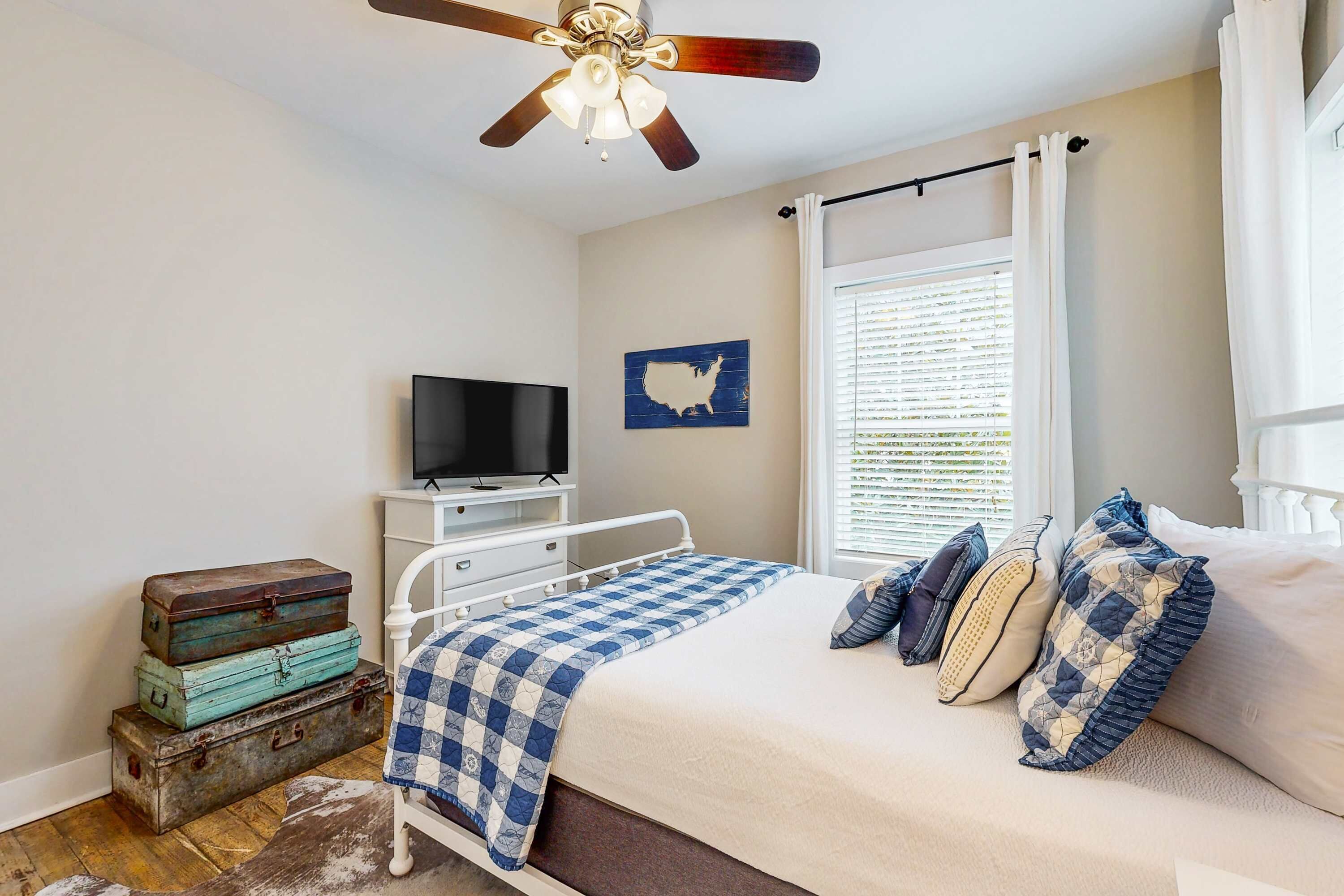 A bedroom with a bed, a television on a dresser, a ceiling fan, and a window with blinds.