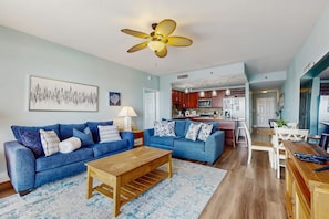 A living room with two blue sofas, a wooden coffee table, and a ceiling fan. - Gorgeous coastal condo with shared pool and private patio (Panama City Beach)