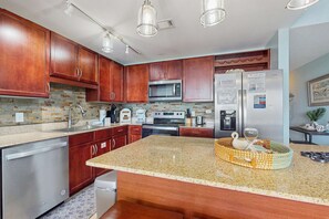 A modern kitchen with wooden cabinets, stainless steel appliances, and a granite countertop. - Gorgeous coastal condo with shared pool and private patio (Panama City Beach)