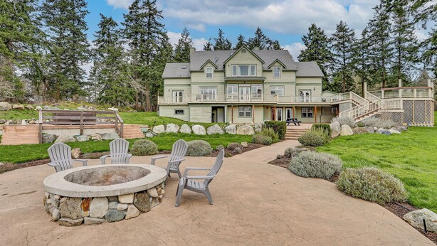 Ein großes, zweistöckiges Haus mit einem Steinkamin und Adirondack-Stühlen im Vorgarten.
