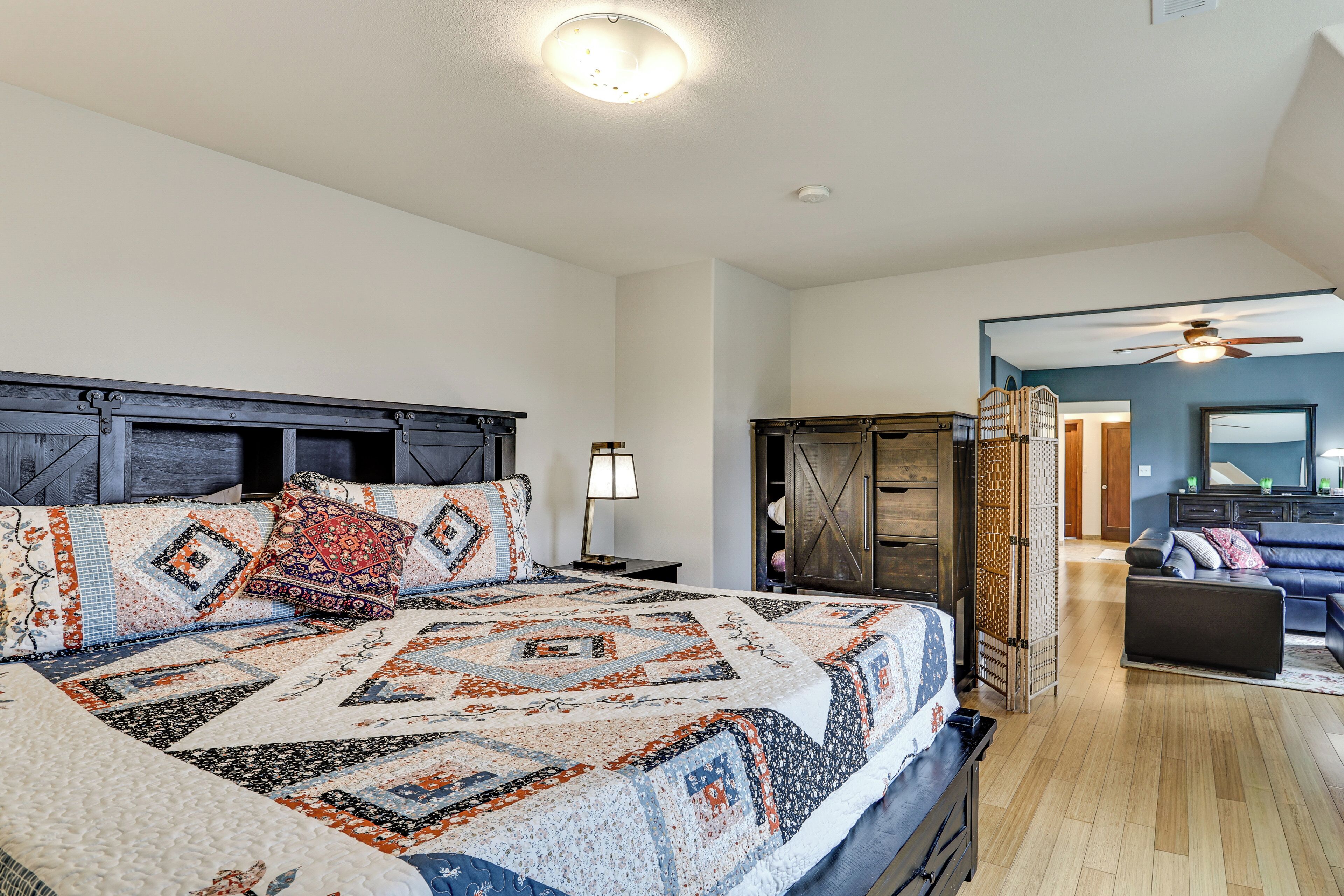 Een slaapkamer met een groot bed, een nachtkastje, een dressoir en uitzicht op de woonkamer.
