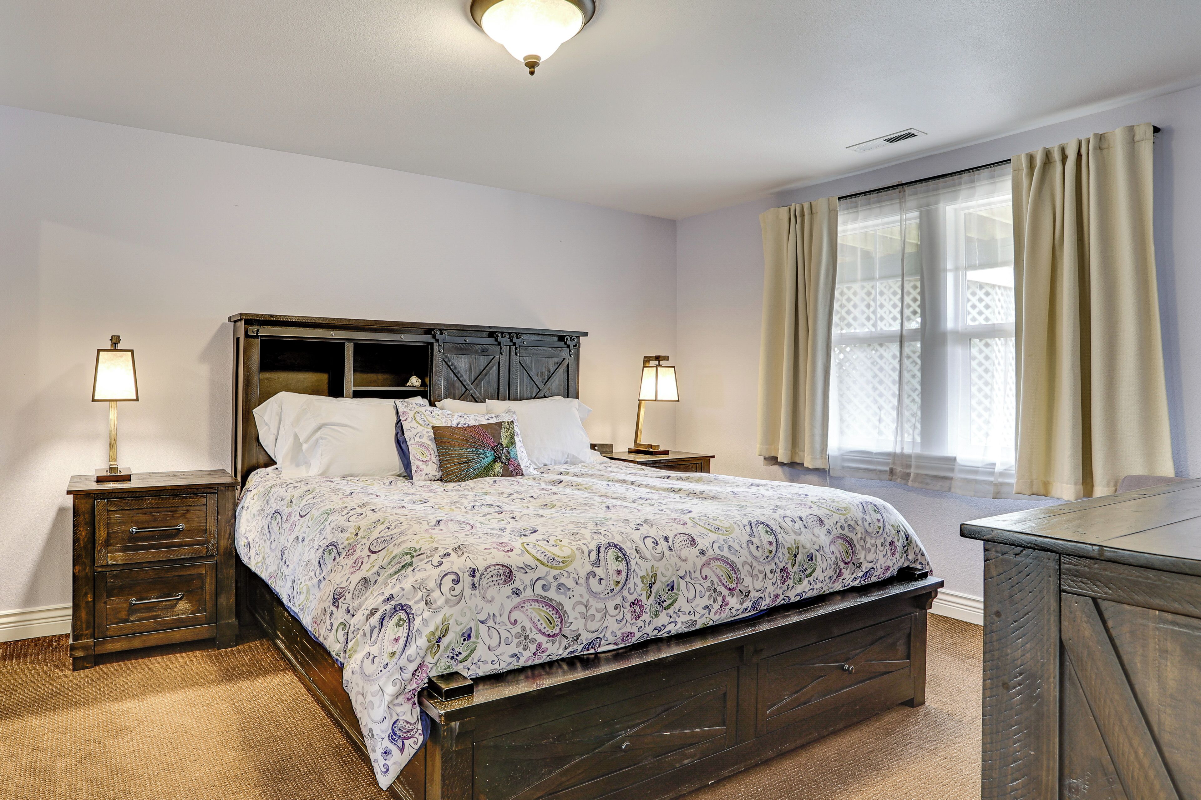 Une chambre à coucher avec un grand lit, deux tables de chevet, une tête de lit en bois et une fenêtre avec des rideaux.