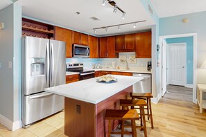 A modern kitchen with stainless steel appliances, wooden cabinets, and a marble island with bar stools. - Spacious condo with bunk beds, rooftop pool, hot tub, washer/dryer & central AC (Panama City Beach)