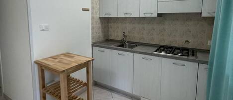 A small kitchen with white cabinets, a wooden table, and a gas stove.