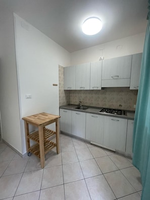 A small kitchen with white cabinets, a wooden table, and a gas stove. - Comfortable Flat With Private Garden in Rosolina (Rosolina)