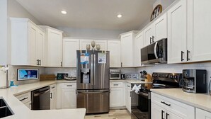 A modern kitchen with white cabinets, stainless steel appliances, and a wooden floor. - Gorgeous coastal home, dog friendly, private hot tub & close to beach (Panama City Beach)