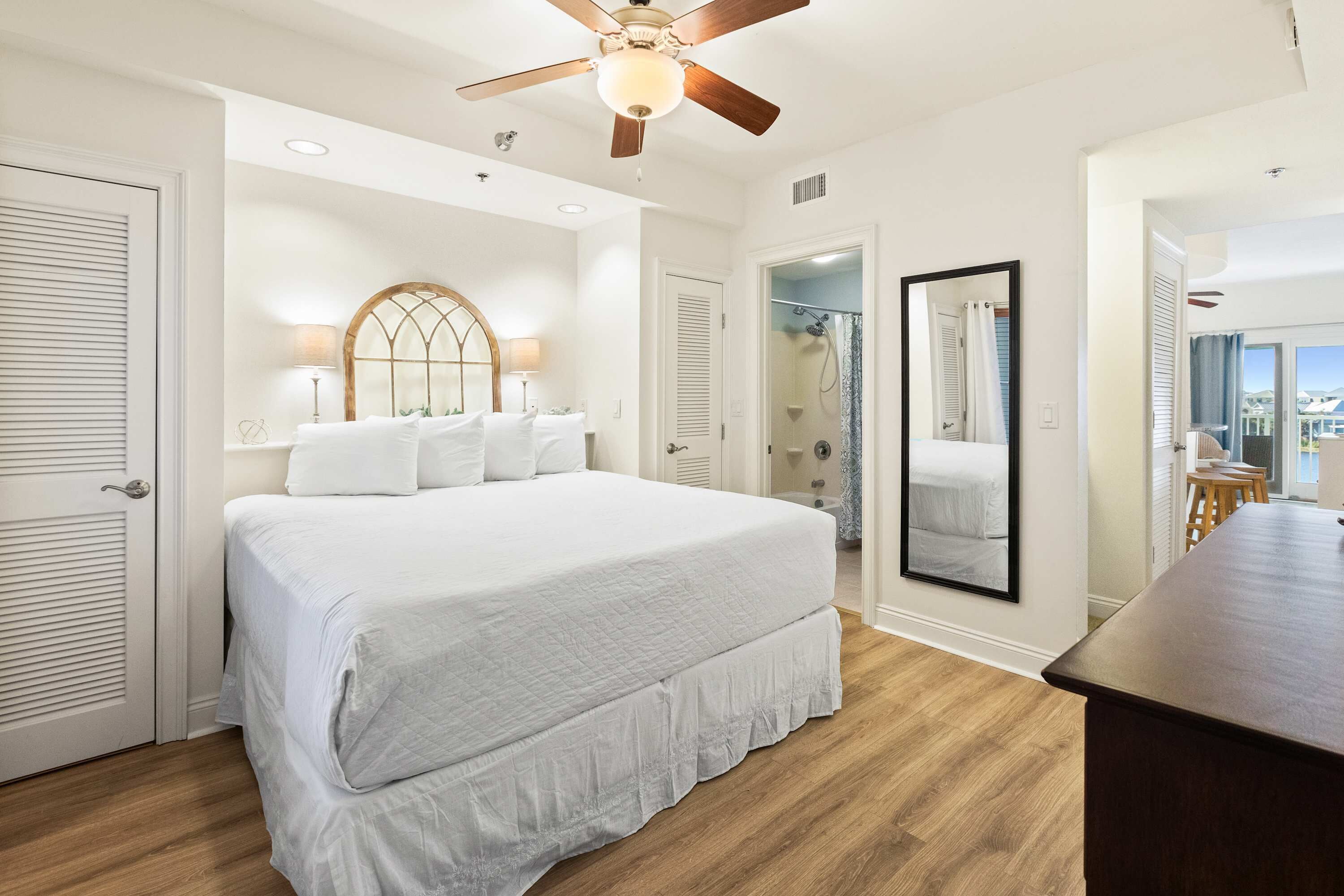Quarto com cama grande, ventilador de teto, espelho e vista para o exterior.