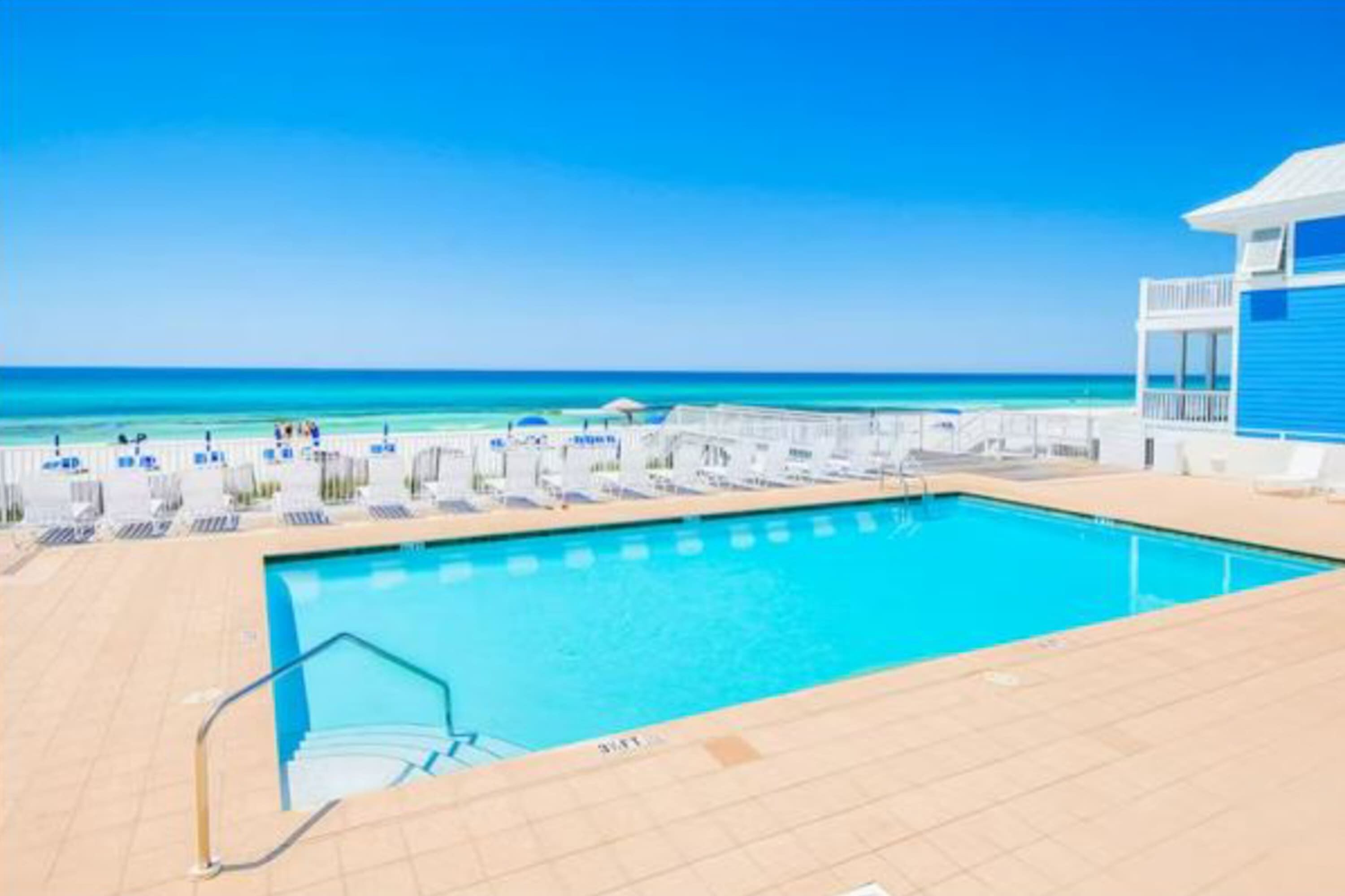 Ein Poolbereich mit freiem Blick auf das Meer, ein Schwimmbecken und ein Gebäude mit blauer Fassade.