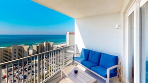 A balcony with a blue sofa and a table, overlooking a beach with buildings in the background. - Gulf View & Laketown Wharf Condo with full kitchen, shared pool and beach access (Panama City Beach)