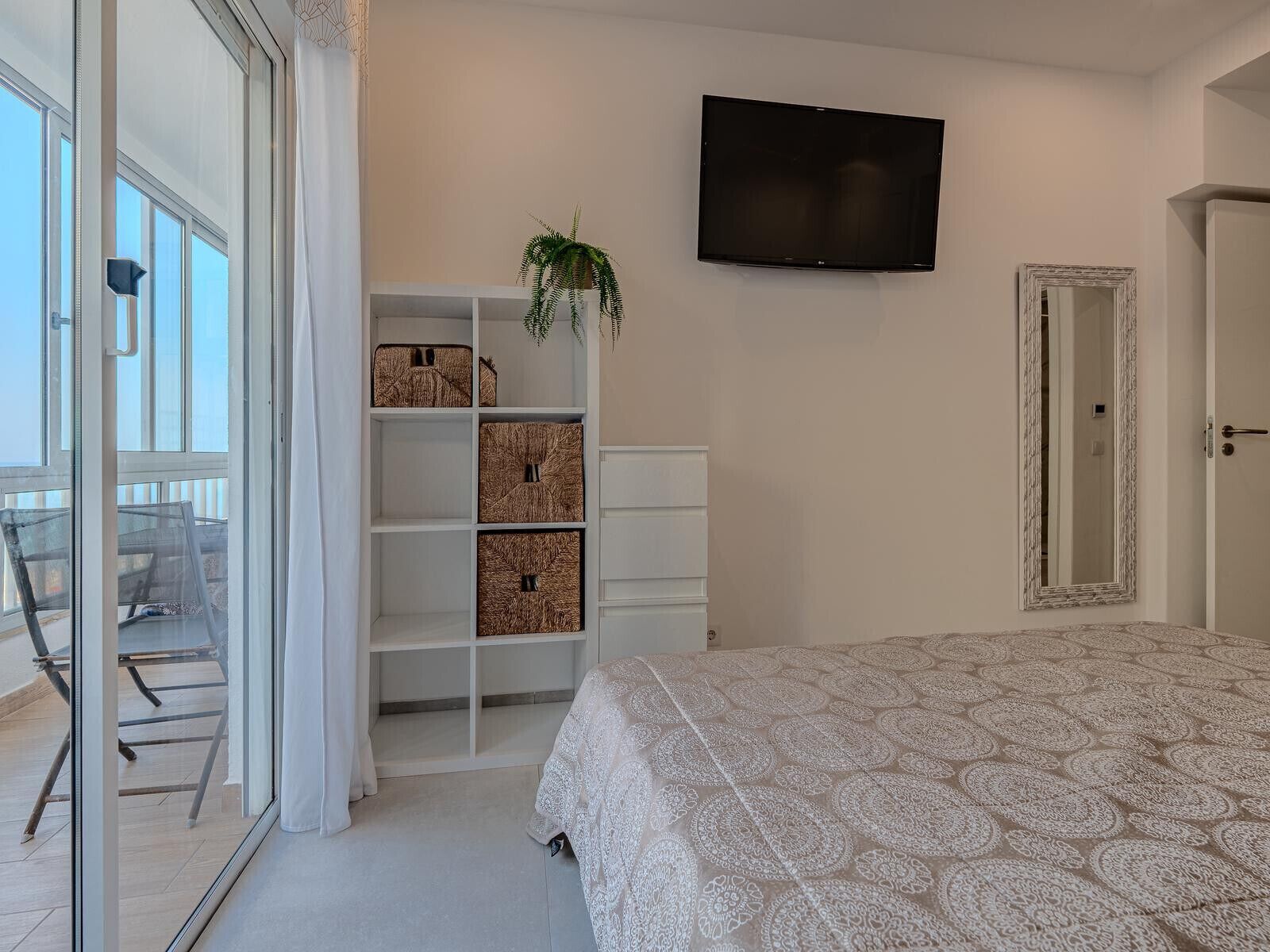 Une chambre avec un lit, une télévision, une armoire et un balcon équipé d’une chaise.