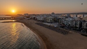 Paisagem costeira com praia, edifícios e um pôr do sol.
