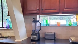 Eine Küche mit Holzausstattung, einem Mixer, einem Toaster und farbigen Glasflaschen auf der Fensterbank.