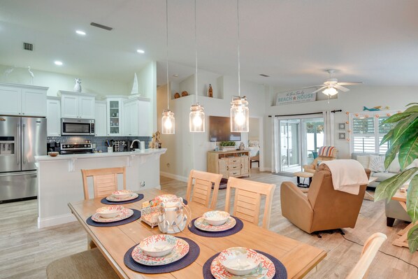 A modern kitchen with white cabinets, a microwave, and a dining area with a wooden table set for four. - Stroll to Shore: Pet-friendly Flagler Beach Escape (Flagler Beach)