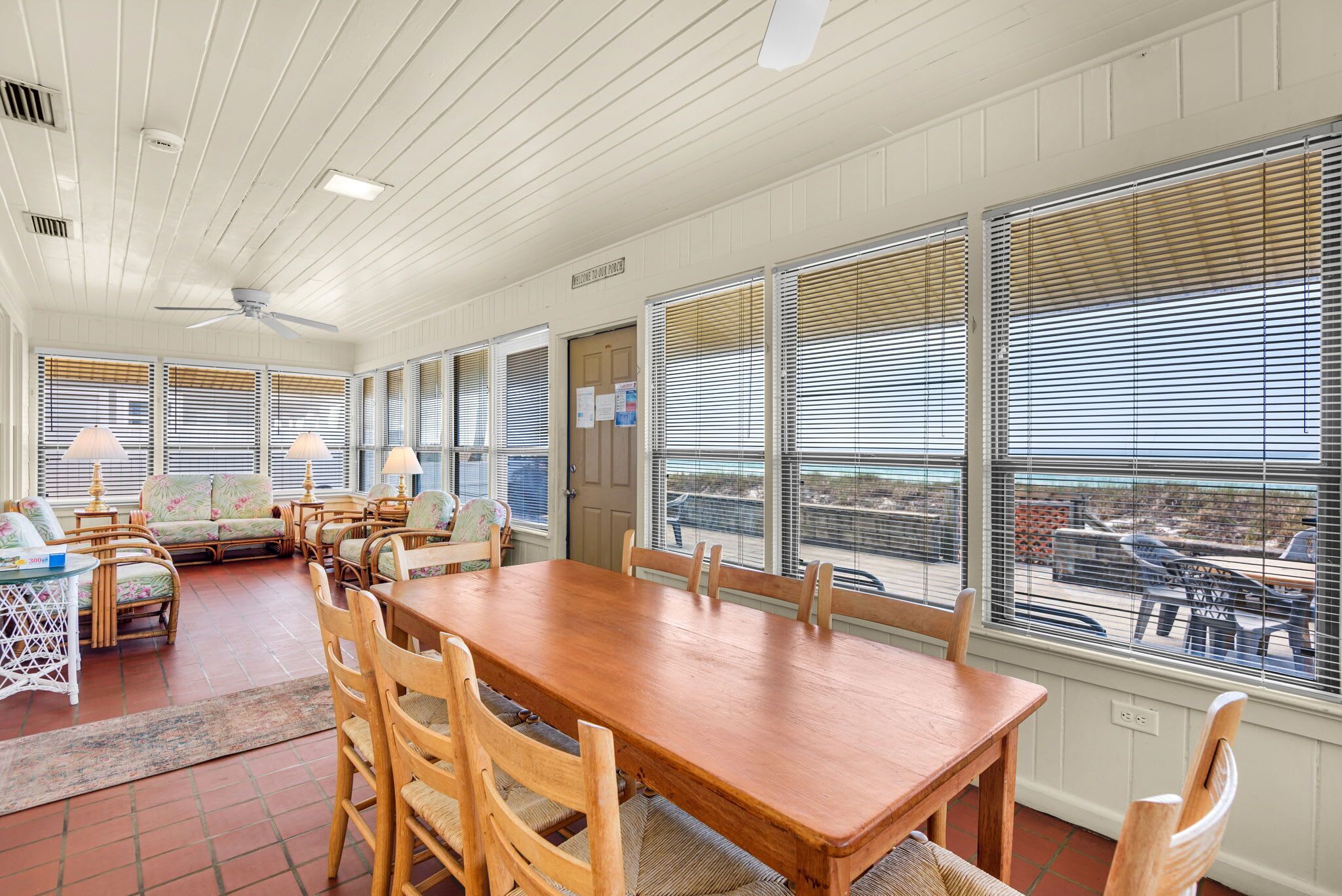 A dining area with a wooden table and chairs, a sofa, and a view through large windows.