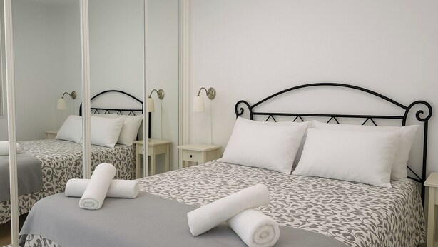 A hotel room with a bed, a bedside table, a mirror, and a lamp. - Miguel Rosas (Las Palmas de Gran Canaria)