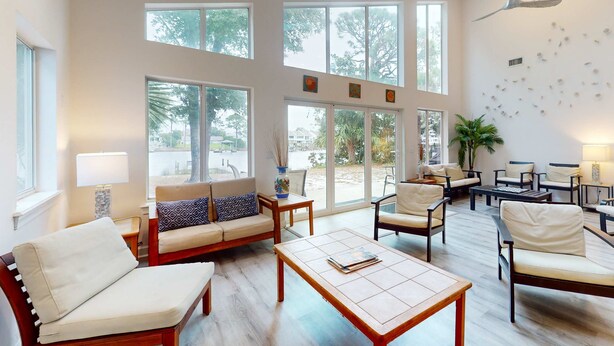 A spacious living area with a sofa, chairs, a coffee table, and large windows. - Lagoon-front home with dock & soaking bathtub (Panama City Beach)