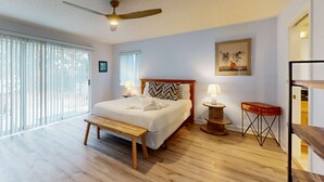 A spacious bedroom with a large bed, a wooden bench, a ceiling fan, and a view through floor-to-ceiling windows. - Lagoon-front home with dock & soaking bathtub (Panama City Beach)