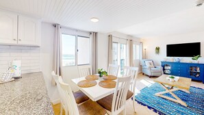 Una sala de estar moderna con comedor, muebles blancos y un ventanal que proporciona luz natural.