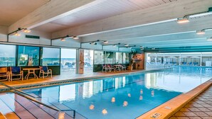 Una piscina interior con agua cristalina, rodeada de sillas de descanso y mesas, y amplias ventanas que ofrecen vistas al exterior.